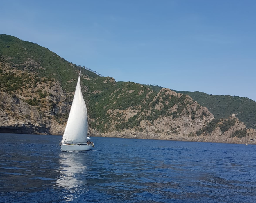 Ein Segelboot auf dem Meer. Im Hintergrund ist eine bergige Küste zu sehen.