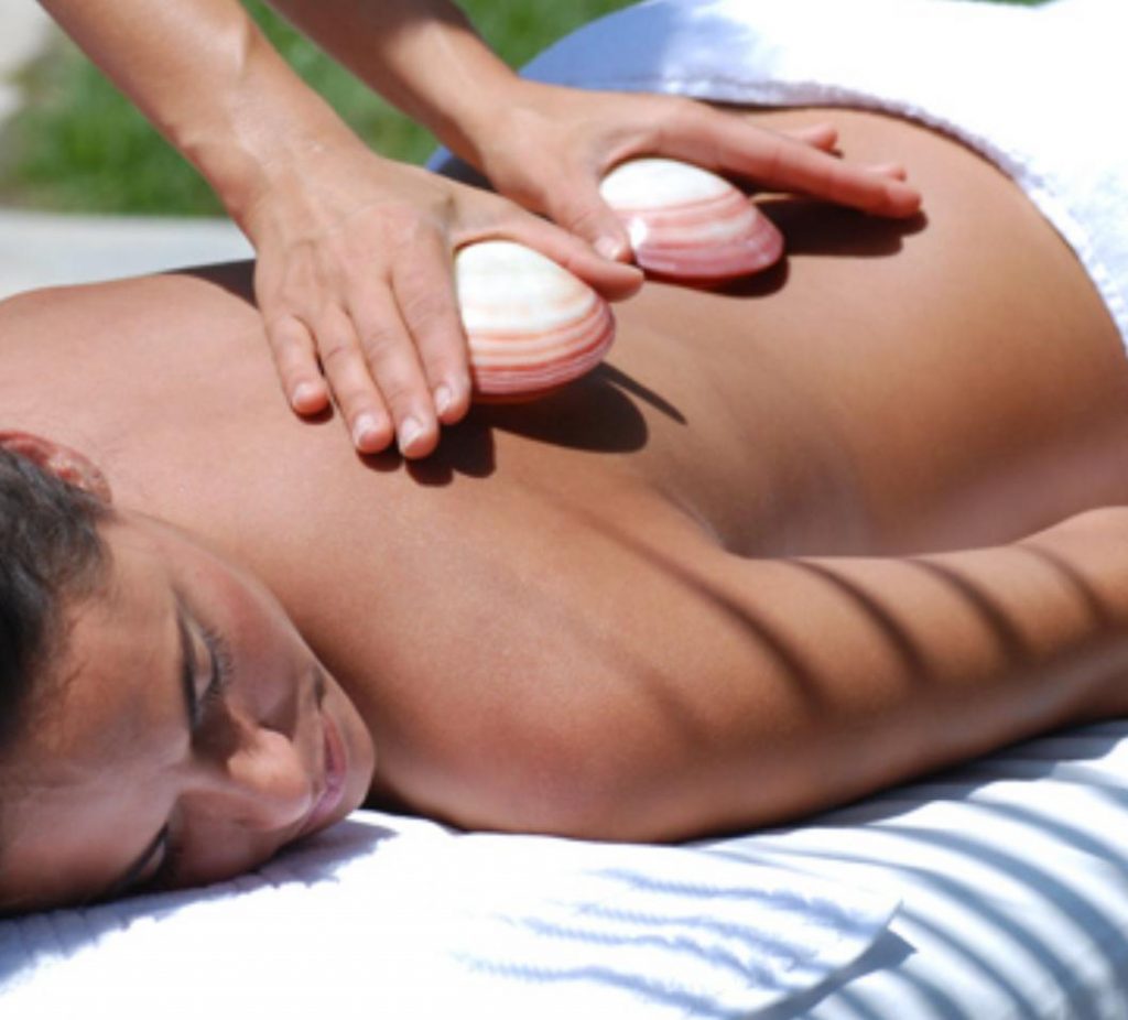 Eine Patientin wird in diesem Bild mit der Hot Shell Massage der PhysioCranio Privatpraxis Dietlinde Liptak in Göppingen - Bartenbach behandelt. Dabei kommen Venusmuscheln zum Einsatz, die bei der Hot Shell Massage essenziell und wohltuend sind.